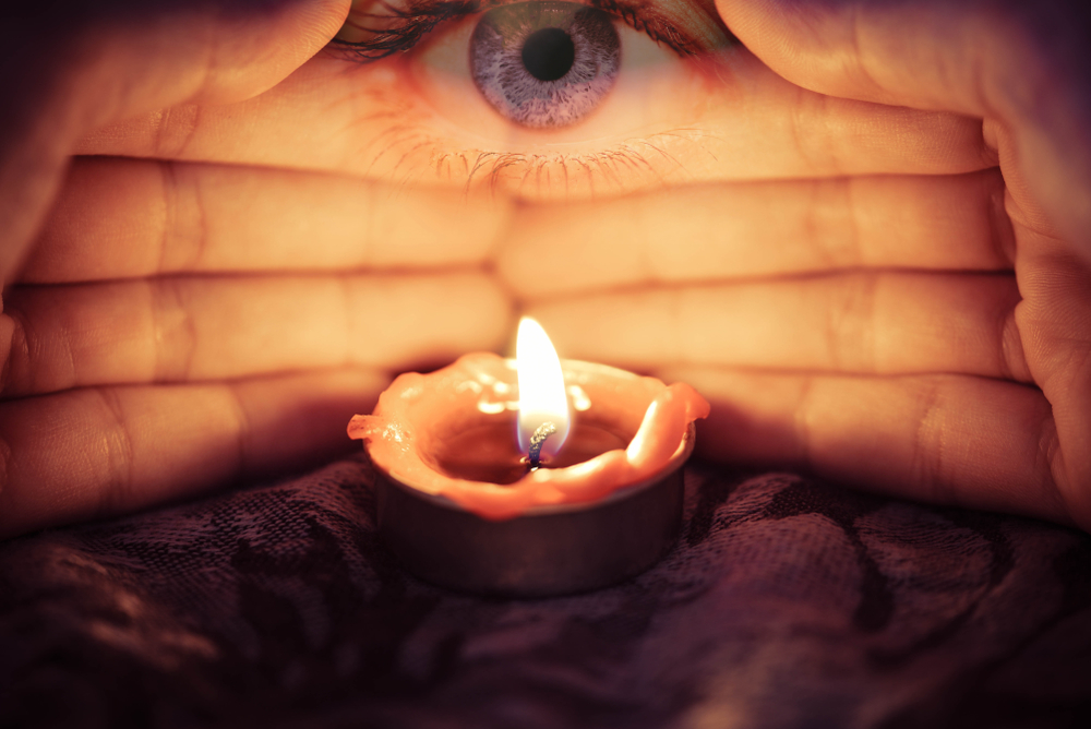 Hand with candlelight burning candle on the darkness background with the eye looking for Astrology Occult Magic illustration / Magic Spiritual Horoscopes and Palm reading fortune teller concept