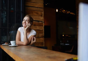 woman-at-coffee-bar-smiling-on-phone-1920w